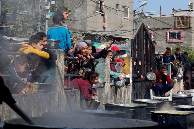 Children wait, some with empty pans in their hands, to receive food cooked by a charity kitchen amid food shortages in Rafah, Gaza.