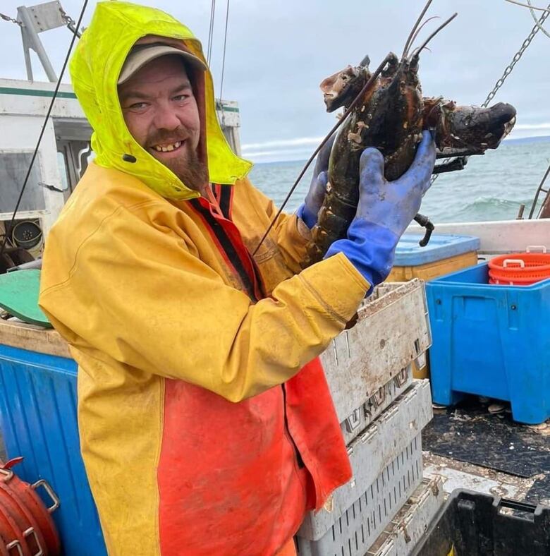 An Indigenous man in fishing gear holds up a lobster 