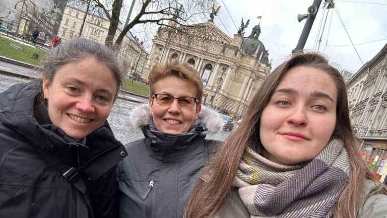 Three women in winter clothing pose in front of a historic building in Ukraine 