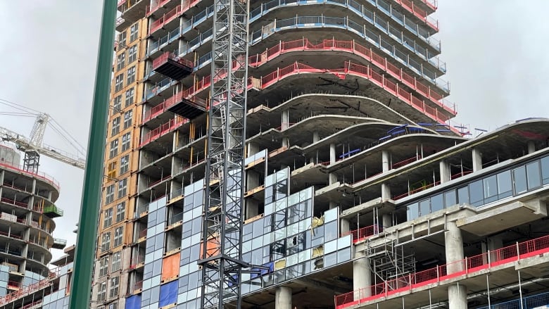 A building is seen with significant damage along its side, with a crane in the foreground.