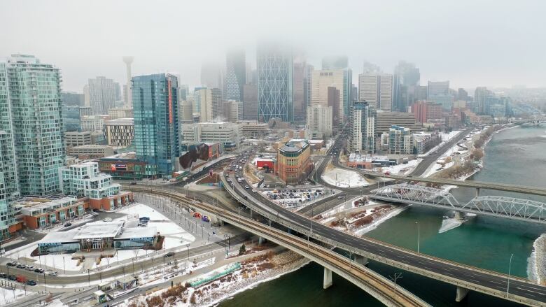 a city skyline is shown on a foggy day by a large river. a few roads pass overtop of the river.