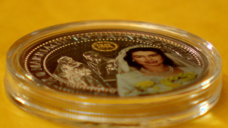 An up close look at a silver coin in a plastic protective covering. The coin contains a photo of a young Queen Elizabeth. 