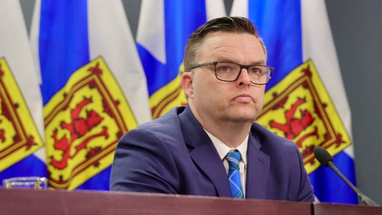 A man with glasses sits as a desk.