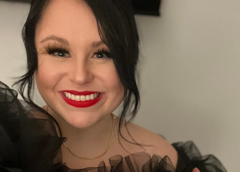 A woman wearing red lipstick and a black blouse poses in front of a white wall.