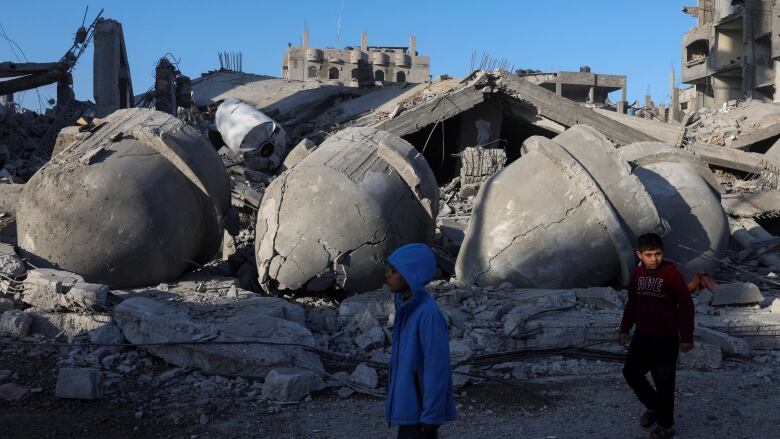 Two children walk past the crumbled, concrete domes of a mosque destroyed in an airstrike. 