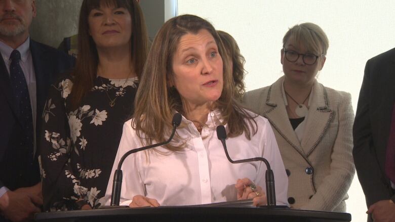 A woman in a white shirt speaks behind a podium.