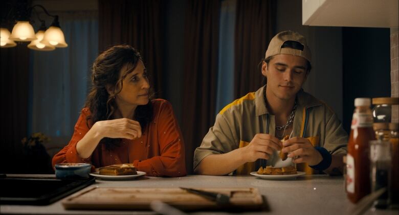 Actress Michaela Watkins is seen in the movie Suze next to actor Charlie Gillespie. They are eating grilled cheese sandwiches at a kitchen counter.