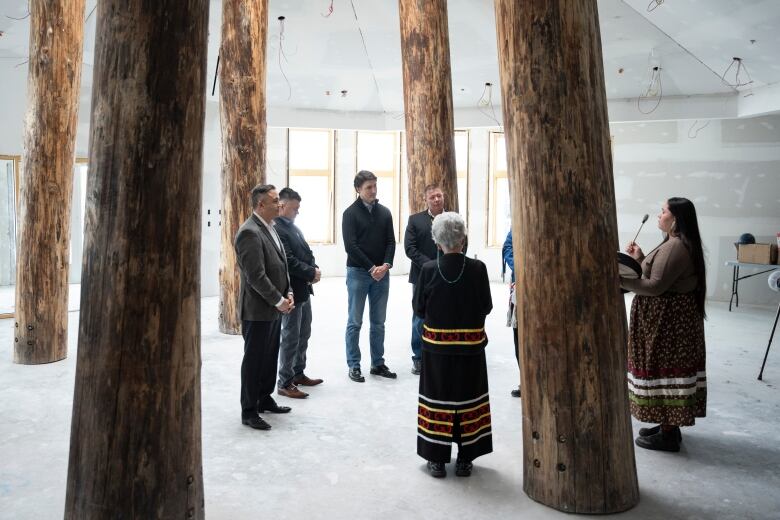 A group of people stand in between large wooden poles in  prayerful poses.