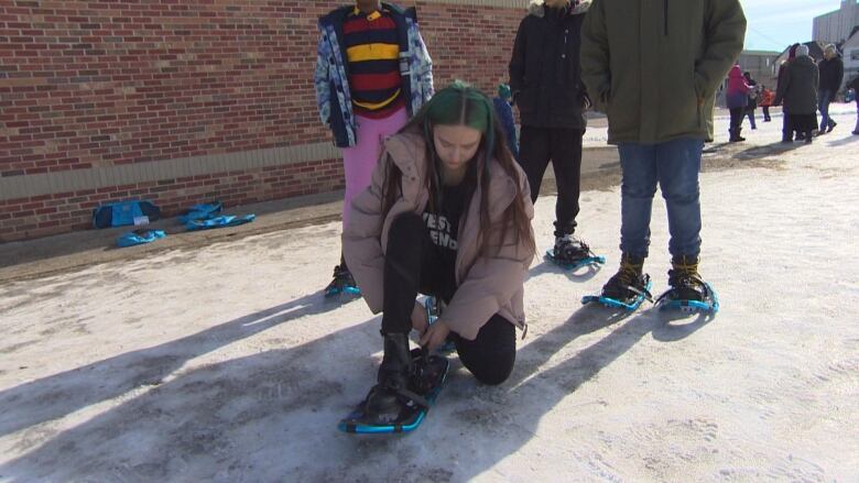 A person puts on a snow shoe. 