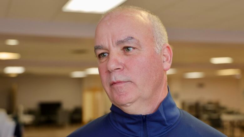 a white man with thinning white hair is seen wearing a navy mock neck zip hoodie