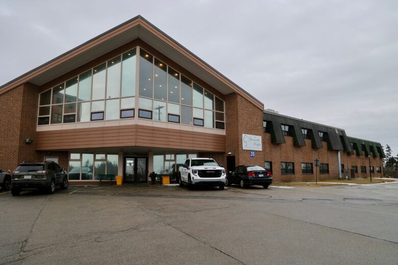 The front of a building, including its entrance is seen with parked cars in front