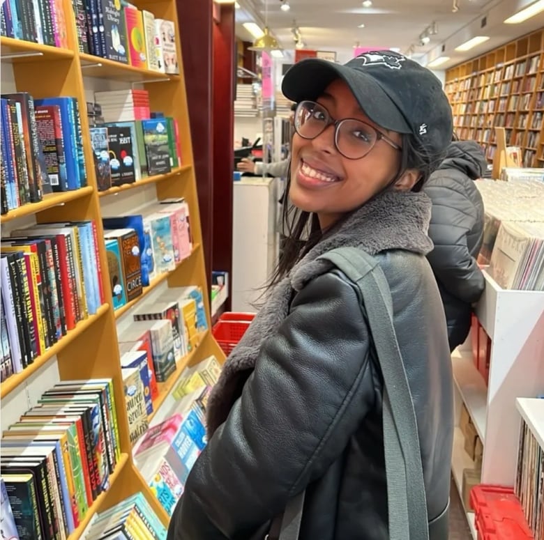 A young woman smiles while standing in an aisle at a book store.