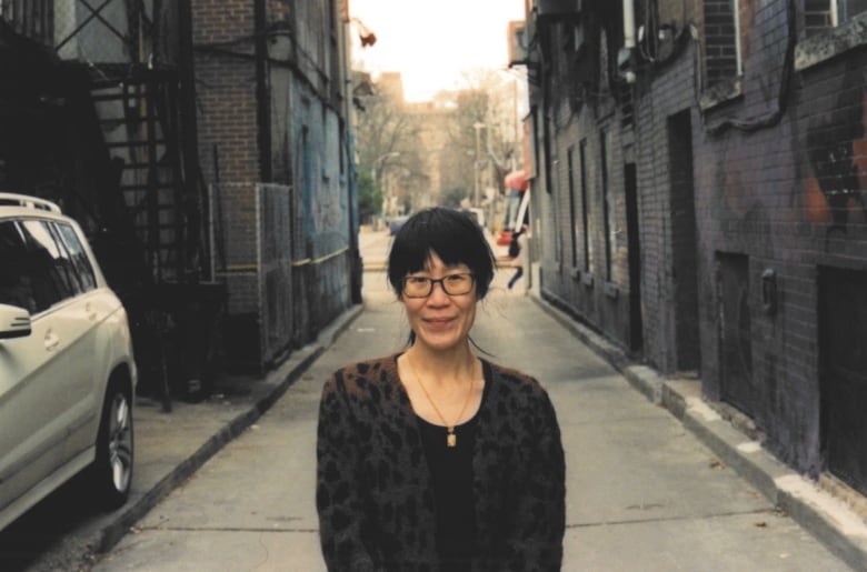 An Asian woman with bangs and a ponytail stands in a Toronto alley.