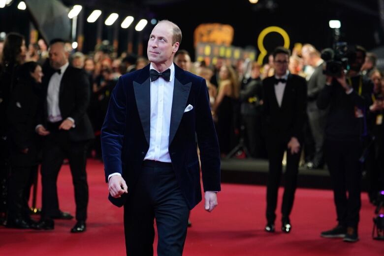 A person walks down a red carpet with other people in the background.