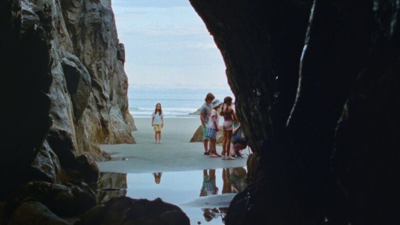 Excerpt from a film with a shot of a group of children at a beach seen from an opening of a cave.