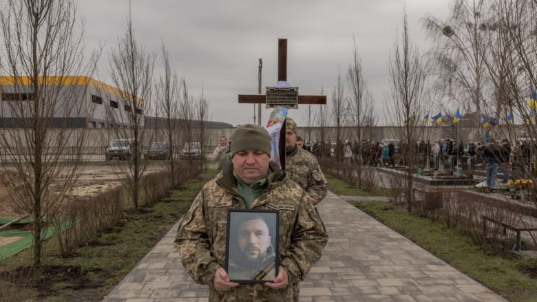 A Ukrainian soldier carries a portrait of late Ukrainian serviceman.