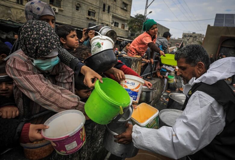 Young people hold out containers to receive food from a worker.