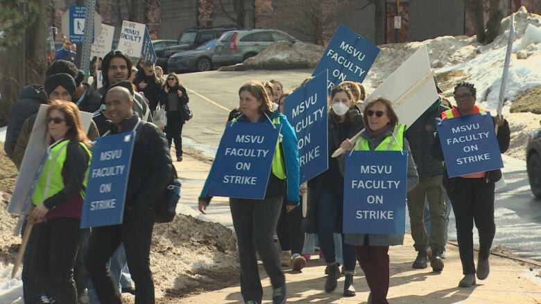 People stand on a sidewalk with signs.