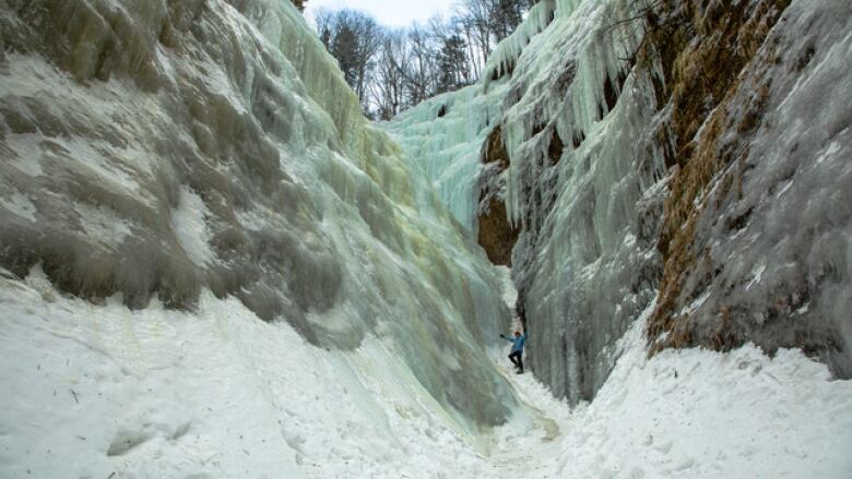 A person dressed in winter gear stands outside in between tall cliffs covered in ice.