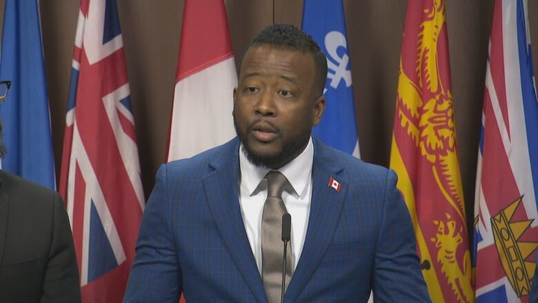 A Black man in a suit speaks to reporters from a podium