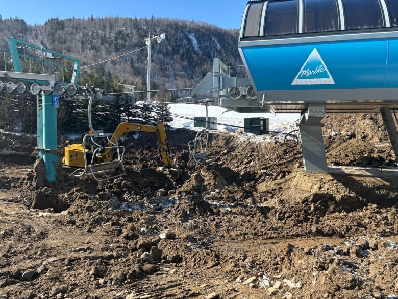 Excavators dig mud out of a large hole formed at the bottom of a ski lift.