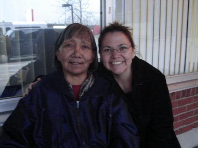 A daughter with her hand wrapped around her mother smiles at the camera.