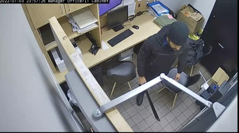 A man in a small office holding a machete.