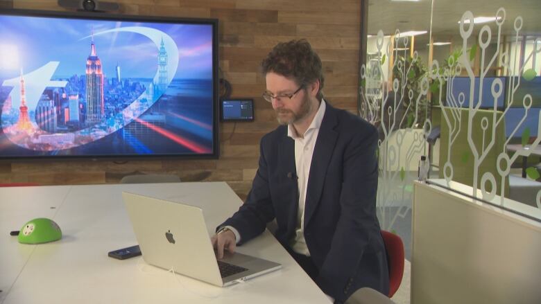 A man in a dark blazer sits at a table, looking at a desktop.