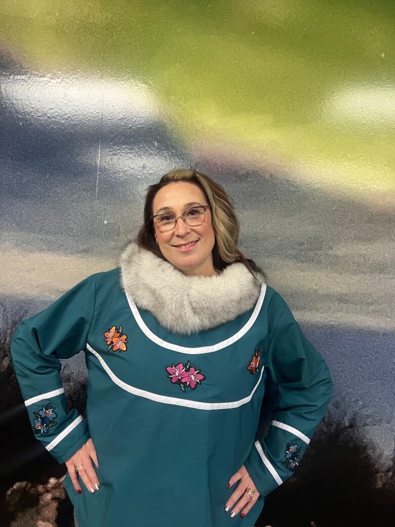 A woman wearing glasses and a blue parka with white fur poses for a photo. 