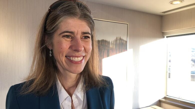 A woman wearing a blue blazer is shown in close-up smiling.