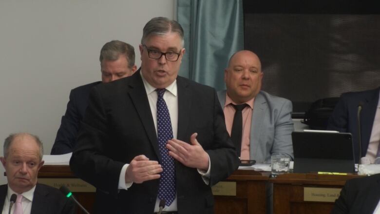 Steven Myers stands in the legislature amongst his cabinet colleagues. 