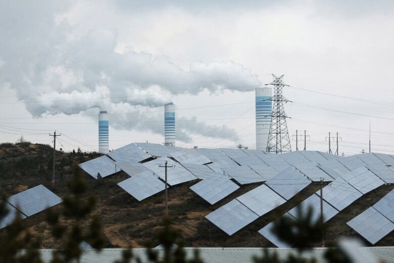 Smoke rises from three chimneys in the background. In the foreground, there are rows of solar panels.