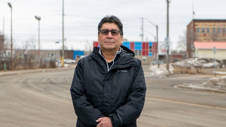 A man in a black jacket stands in a determined pose, on a Thunder Bay street. 