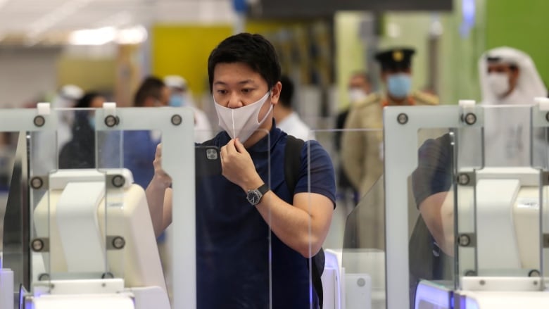 Man wearing a face mask stands behind clear, plastic gates. He is taking a photo of the gates.