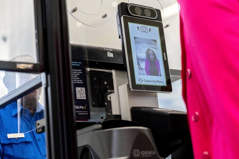 A screen with two cameras displays the image of a woman standing in front of it.