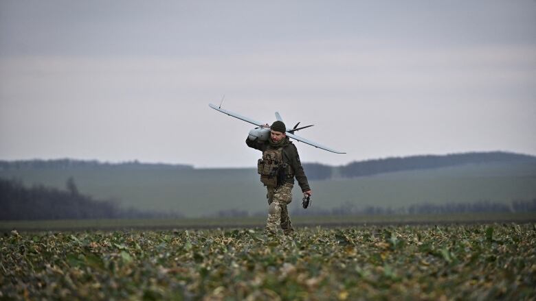 A Ukrainian soldier walks through a field carrying a reconnaissance drone 