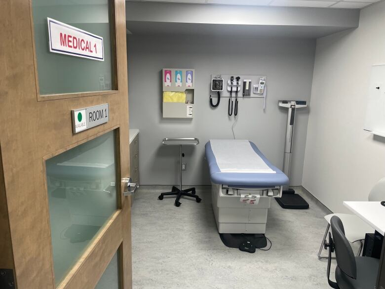 A room in a medical clinic is empty and brightly lit. There is a table with paper on it for patients to sit and lie down on. The room is new and clean.