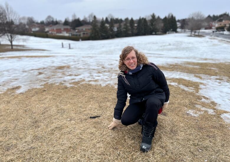 A journalist kneels on a small hill in a park in late winter.