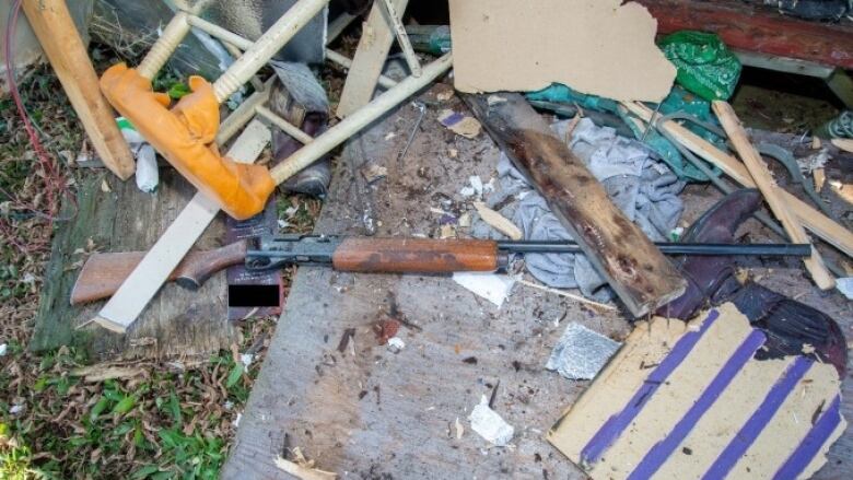 A brown and black .22 rifle lies amid debris outside. 