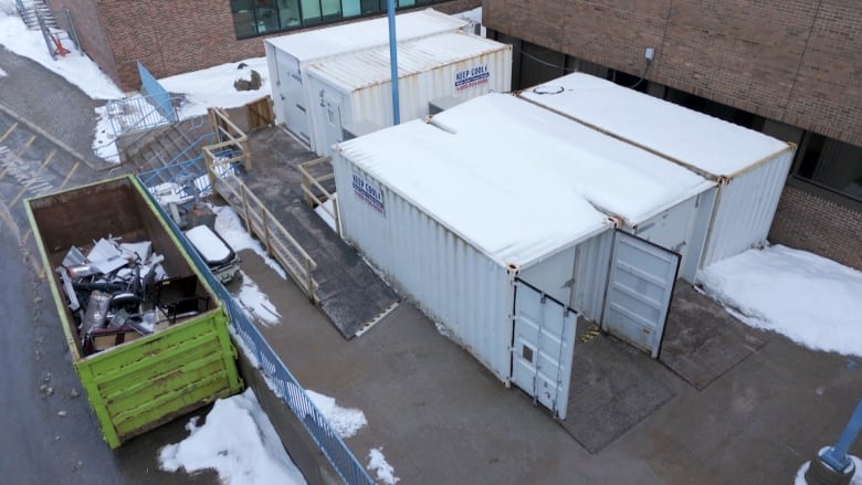 Five white trucking containers are placed on a concrete slab. A green dumpster is next to them. 