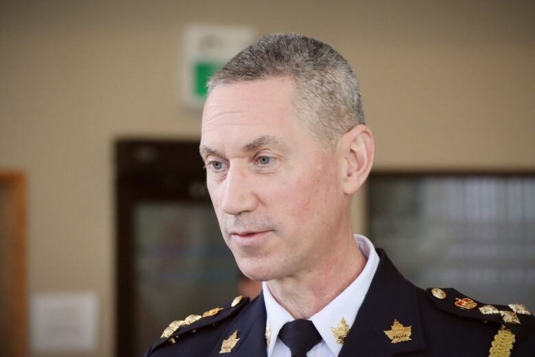 A man with short grey hair wearing a navy blue uniform with gold and badges and buttons speaks to someone who is off camera.