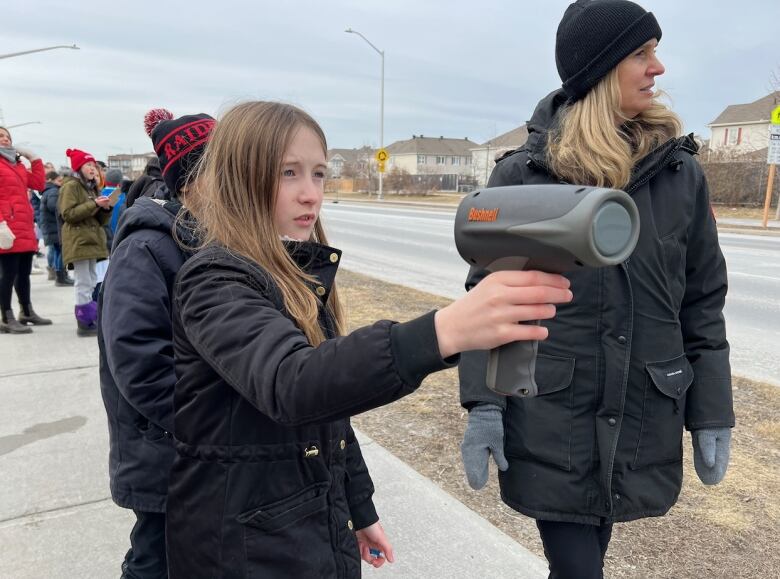 A child holds aims a radar gun at traffic along the road in front of her school