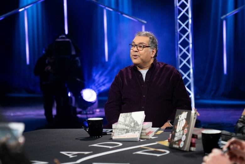 A man wearing a purple button-down sits at a round table. 