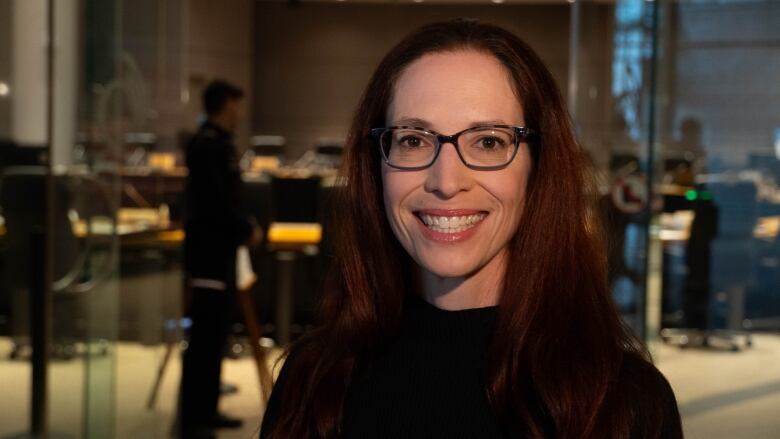 A woman with red hair and dark glasses smiles broadly