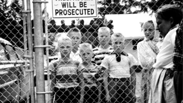 A black-and-white picture of a number of children held behind wire mesh fence.