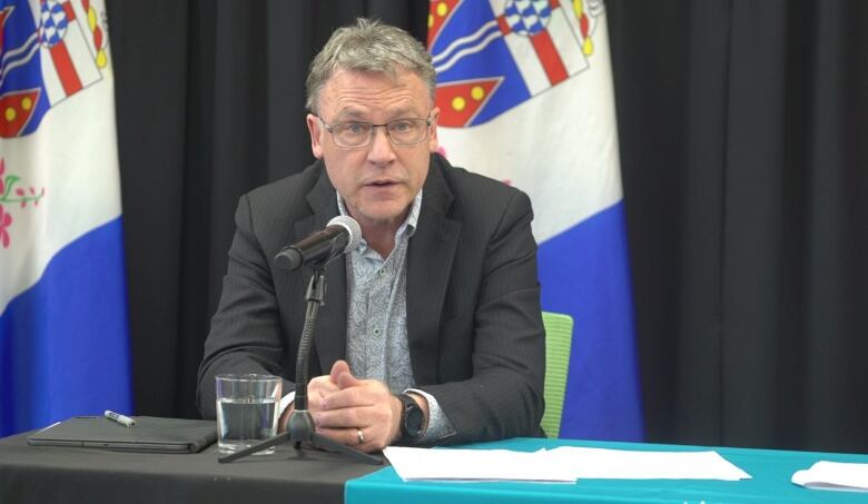 A man sits at a table speaking into a microphone.