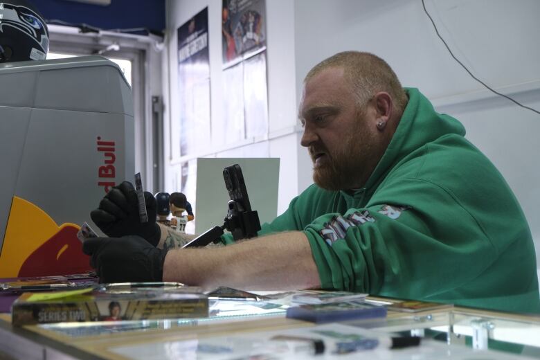 a person in a green hoodie is opening a hockey card package with his phone propped in front of him filming the opening