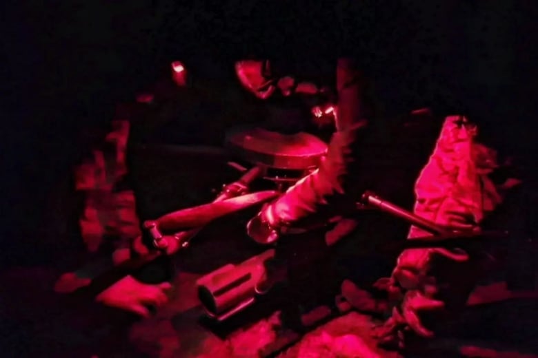 Men attach equipment to a drone under red lighting in a dark room.