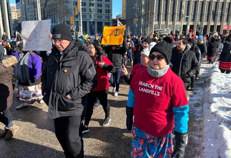 People holding signs calling for a landfill search walk down a downtown street