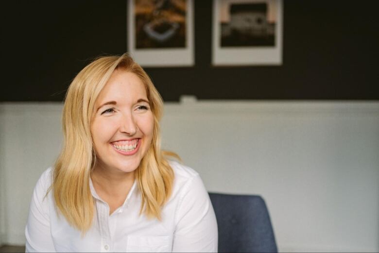 A smiling person with long blonde hair sits in an office space.